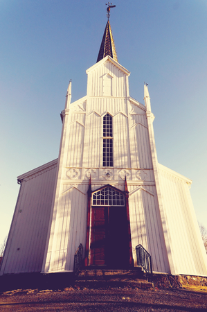 The entrance to the Norwegian Protestant church. Soaring tower, a small white window. Wooden walls, painted white. The sun low on the horizon. Vintage view. Norwegian winter. Gjerstad in Aust-Agder region of Ostlandet. Eastern Norway.の写真素材