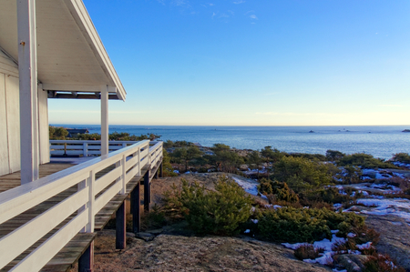 Aerial view of the terrace of the North Sea. Wooden terrace at the campground. The sun low on the horizon in the background of blue sky. Winter scenery, snow on the rocks. Coniferous forest around. Kragero, Telemark municipality. Region of southeastern Noの写真素材
