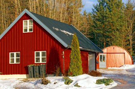 Red wooden garage in winter. Around the tree without leaves. The sun low on the horizon. Coniferous forest around. Kragero, Telemark municipality. Region of southeastern Norway. Skagerrak coast.のeditorial素材