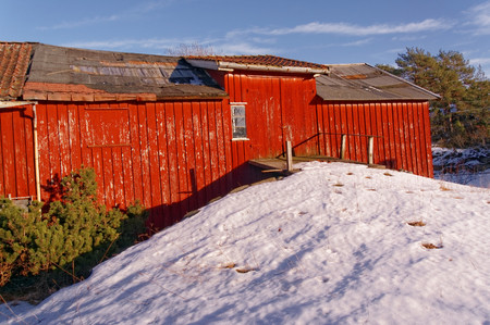 The entrance to the second floor of the barn. Big red barn, wooden wall decor. Destroyed the roof of the building. Farm in winter. Winter scenery, snow on the rocks. Coniferous forest around. Kragero, Telemark municipality. Region of southeastern Norway. のeditorial素材
