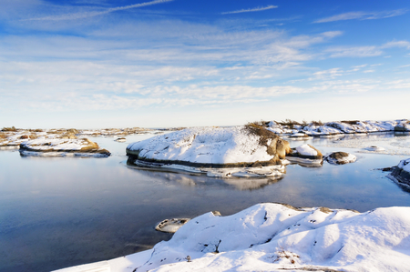 Small rocky islands sprinkled with snow during low tide. Frozen water of the fjord covered with a thin layer of snow. Around the island in the bay fjord covered in ice in the winter. Wavy rocks covered with snow. In the background of the North Sea. Visiblのeditorial素材