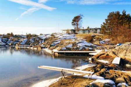 Bay fjord covered in ice in the winter. Wavy rocks covered with snow. In the background of the North Sea. Visible signs of outflow of the sea. Blue sky. Winter in Aust-Agder municipality. Region of southeastern Norway. North Sea Coast. Skagerrak coastlineのeditorial素材