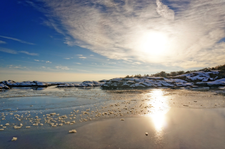 White clouds in a blue sky. Sunset behind the white clouds over the fjord. Around the undulating rocky coastline. Snow on the rocks. Frozen water. Broken ice floes.のeditorial素材