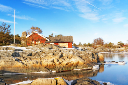 Summer wooden cottage hidden for guests. Around the undulating rocky coastline. Snow on the rocks. Frozen water. Broken ice floes. Blue sky over everything. Skagerrak coastline. Norwegian landscape.のeditorial素材