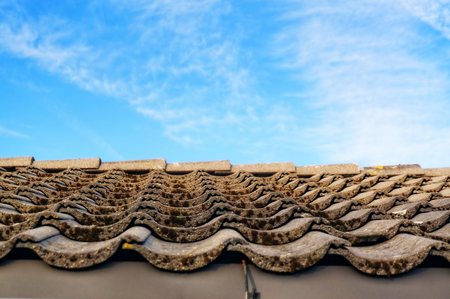 Roof with gray tiles on the tabs on background of blue sky. Gray tiles covered with moss, on a...