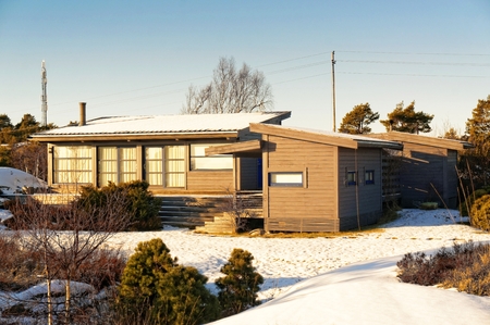 Norwegian coast vegetation surrounds the gray cottage with a big green terrace. Around the spruces,...