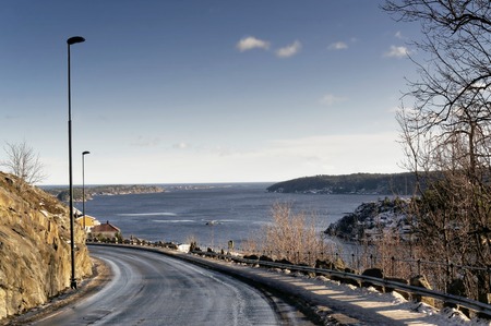 Asphalt road, gravel sprinkled over the fjord. The road under the rocks. A view of the fjord and the North Sea from the top. Windy day. Norway - February 2015.のeditorial素材