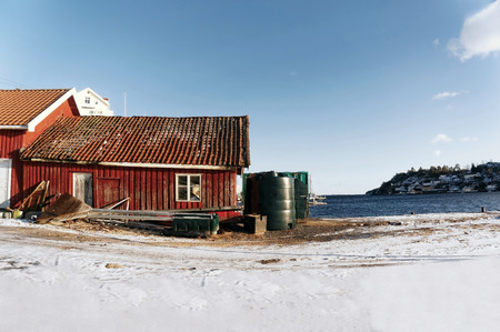 Kragero, Telemark. Norway - February 2015. Red wooden house fisherman. Building on the fjord. Around snow. Water fjord and cottages on the island in the distance.のeditorial素材