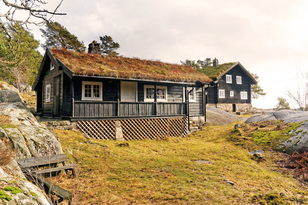 Stabbestad, Telemark. Norway - February 2015. Old brown wooden building sleeping area for guests. In the background traditional norwegian wooden cootage. Rock around the fjord in early spring.のeditorial素材