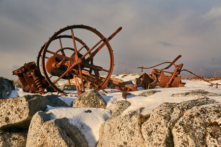 Rural abandoned equipment. Winter landscapes on a small Norwegian island. Snow on the dry grass. High rocks.の写真素材
