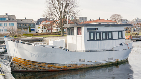 Kristiansand, Norway - June 4, 2015: Old Wooden fishing boat in the bay. Colorful wooden buildings. Bay in Kristiansand.のeditorial素材