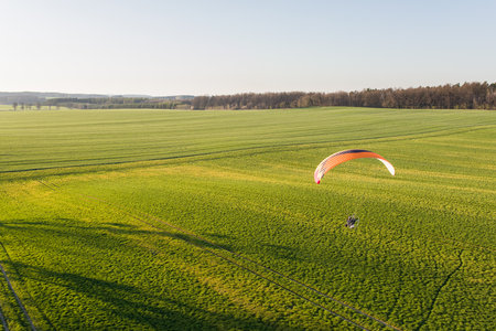 Aerial view of a paraglider flying over a green fieldの写真素材