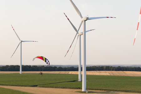 Paraglider flying in the air over a field with wind turbines