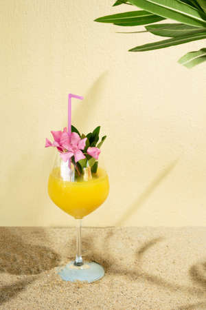 tropic drink on a summer beach with sandy background.green branch making shadow.yellow and pink vibrantの写真素材