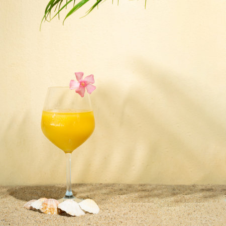 cold yellow drink on a sandy beige background with shells and pink tropic flower on it.summer sunny concept with shadowsの写真素材