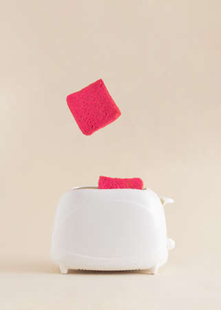 Pink toast coming out of toaster on a soft bright beige background.Morning breakfast  abstract creative idea.Happy surprise foodの写真素材