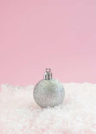 Metallic silver shiny bauble on a snow.Soft pink background.Christmas aesthetic design.New Year conceptの写真素材