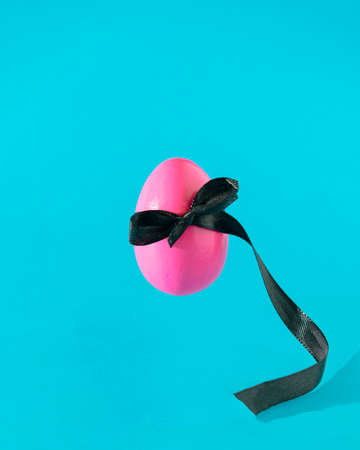 Egg pink with black bow flying on a sky blue background. Easter aesthetic design idea. Present holiday concept.の写真素材