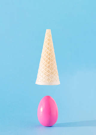 Egg pink dropped out of ice cream cone flying above. Easter aesthetic food design concept idea. Holiday spring sunny momentの写真素材