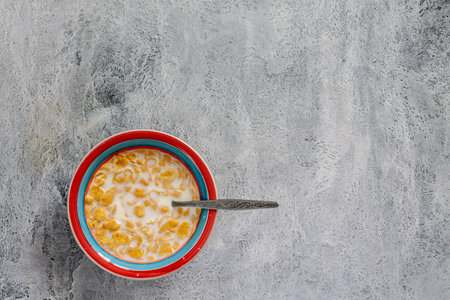yellow cornflakes with milk in a multicolored plate on a gray background. Healthy breakfast