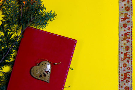 a red notepad lies on a yellow background, a metal toy with the inscription merry christmas lies on the notepadの写真素材