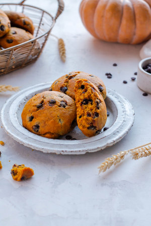 oatmeal cookies with chocolate chips in a plate on a white background, next to it lies an orange pumpkin and ears of wheatの写真素材