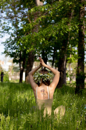 a girl with blonde hair and a wreath of flowers meditates in nature in the tall green grassの写真素材
