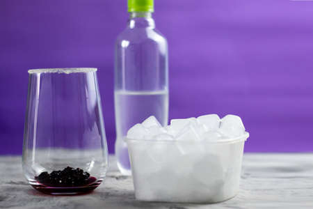 Making a cocktail at home. A glass of jam, soda and ice are on the table. Purple background. Multicolored iceの写真素材