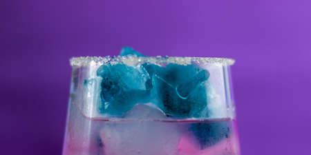 Making a cocktail at home. A glass of jam, soda and ice are on the table. Purple background. Multicolored iceの写真素材