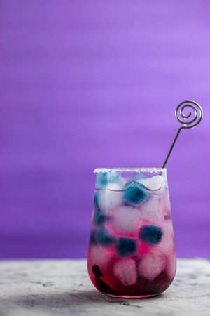 pink cocktail with blueberries stands on the table. There is blue and blue ice in the glass. Purple background. Place for text.の写真素材