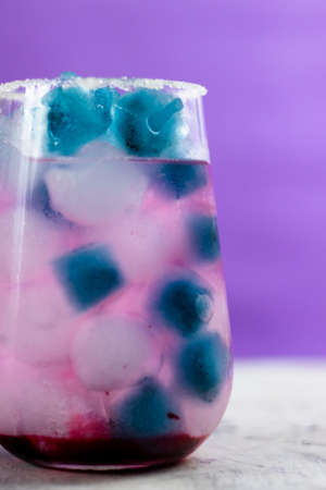 pink cocktail with blueberries stands on the table. There is blue and blue ice in the glass. Purple background. Place for text.の写真素材