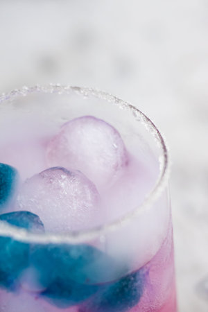 pink cocktail with blueberries stands on the table. There is blue and blue ice in the glass. Purple...