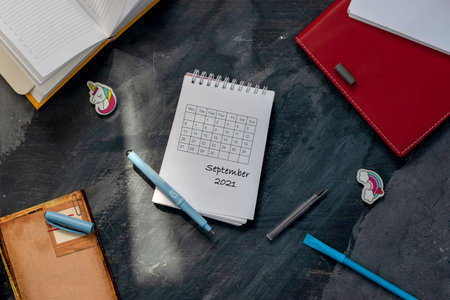 September 2021 calendar written in a notebook that lies on a gray background surrounded by office and school suppliesの写真素材