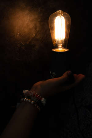 female hand holding a switched on lamp on a black backgroundの写真素材