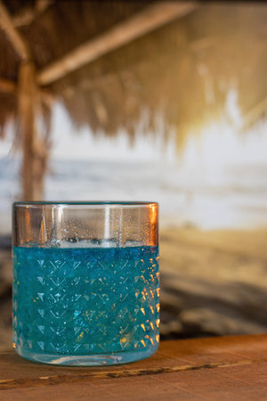 A blue summer cocktail stands on a wooden bar on the beach. sunset raysの写真素材