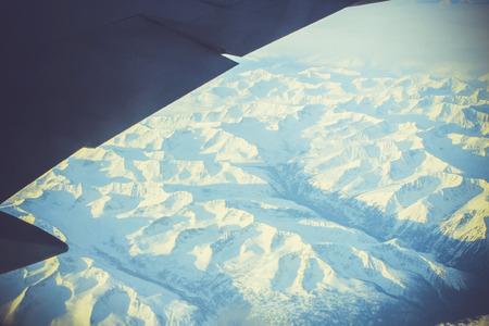 Wing of the plane on blue sky background and snowy mountains, view from windowの写真素材