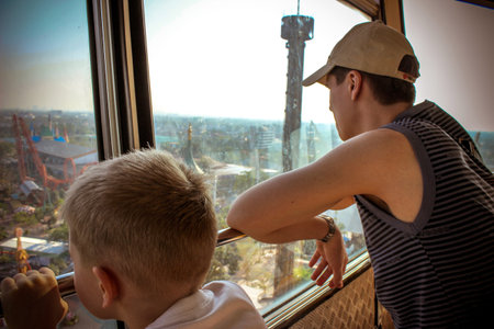 father and son looking out the window at high altitude in amusement park
