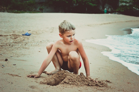 young boy playing in sand and waves on the beachの写真素材