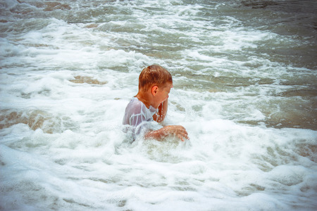 boy at the sea lying in sand and wavesの写真素材