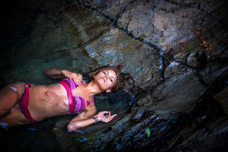 Beautiful sexy model posing in water of waterfalls wearing bikini swimwear at summer timeの写真素材