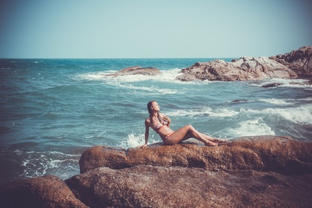 Young sexy woman in red bikini posing In front of sea on the stones and splashes water. Koh Samui beachの写真素材