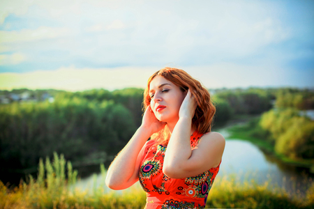 Young red-haired woman on the rock near river is fashionable posesの写真素材