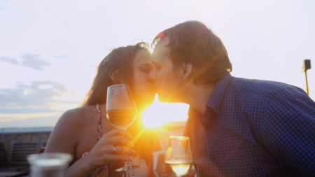 Beautiful couple in love on romantic date at beach restaurant  sunset kissing with sunny lense flare effects.の写真素材