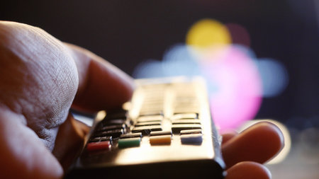 Close up of womans hand with a television remote control on blurred background at sunset timeの写真素材