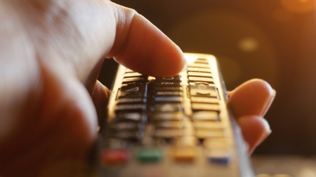Close up of womans hand with a television remote control changing channels at sunset time  lense flare effectsの写真素材