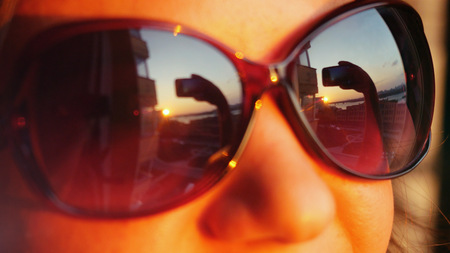 Close up of view smiles womans face in sunglasses holding smartphone takes picture on sunset in the city background. That reflected in herの写真素材