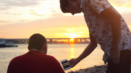 Young man shows something on his mobile phone other guy at beautiful sunsetの写真素材