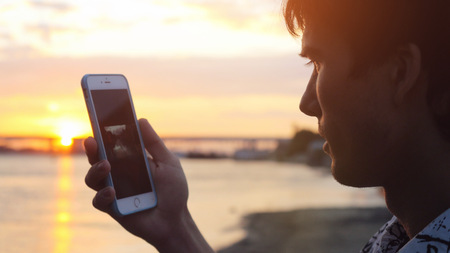Man uses smart phone at beautiful sunset on the beachの写真素材