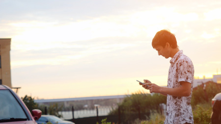 Young handsome man using smartphone outdoors at beautiful sunset time. Businessman walking on the city background through the sun with lense flare effectsの写真素材