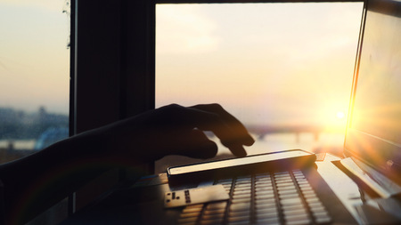 Woman shopping with her laptop on blurred city background during amazing sunset and beautiful sun lense flare effectsの写真素材